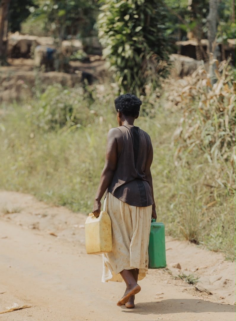 A woman walking away along a rural path with two water containers