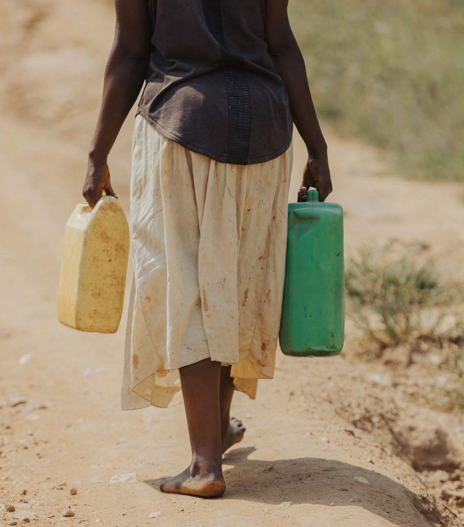 A woman carrying two water containers along a dusty road
