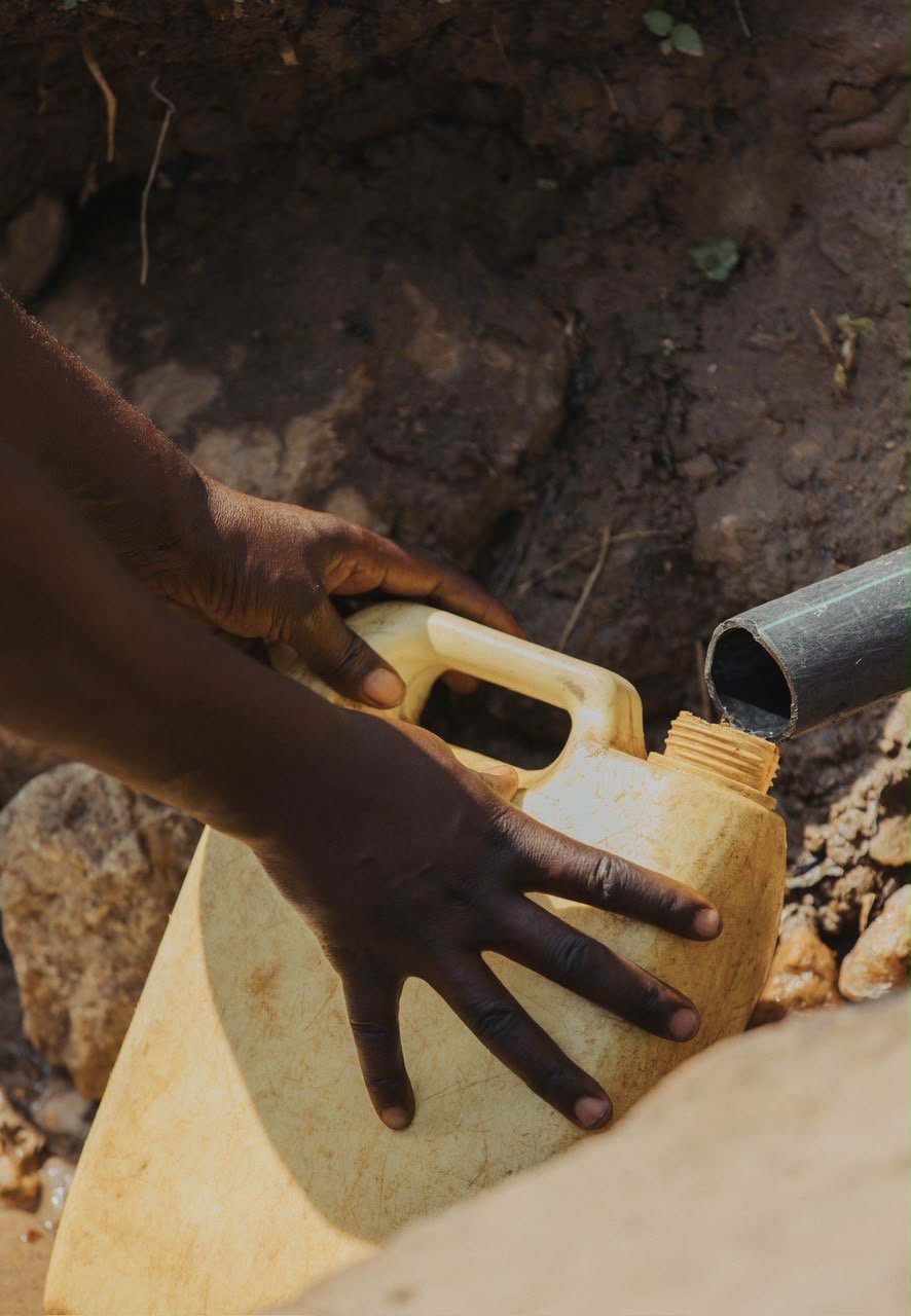 Hands filling a yellow water container from a pipe