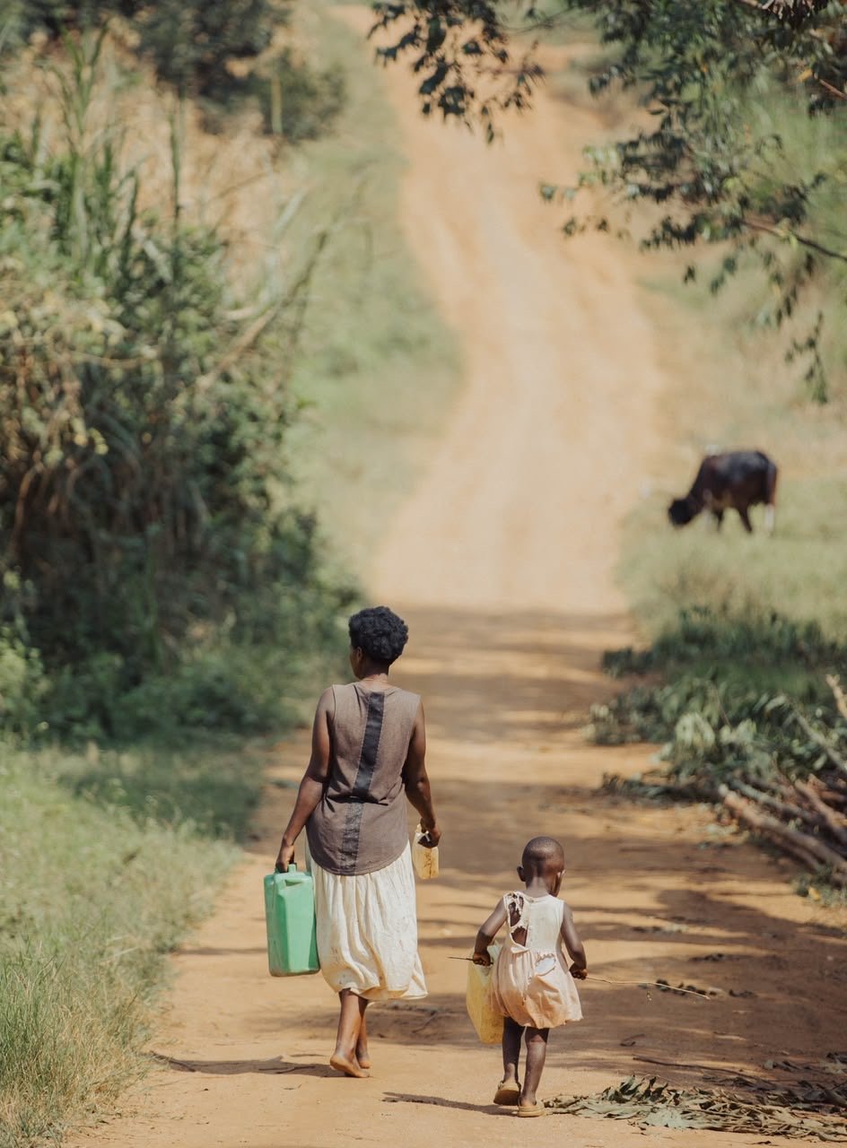 A mother and child walking along a rural road carrying water containers