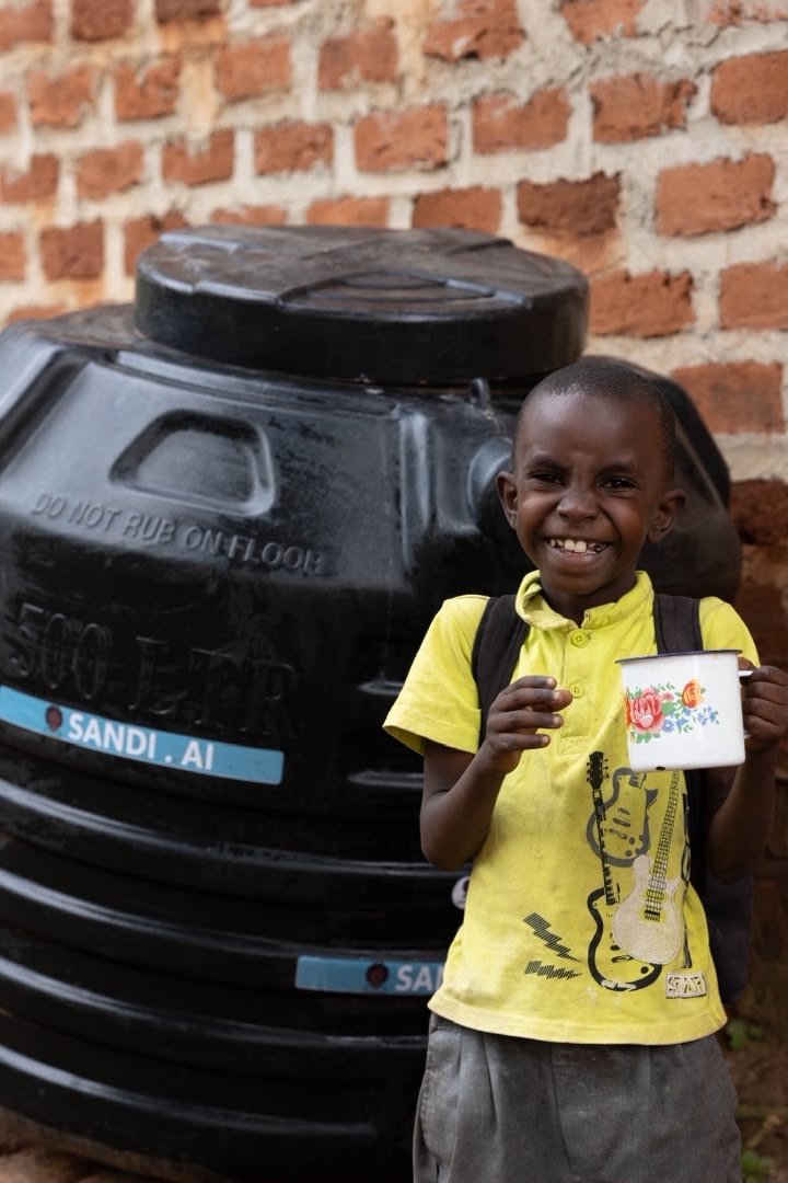 A smiling child holding a cup beside a SandiLyt water tank