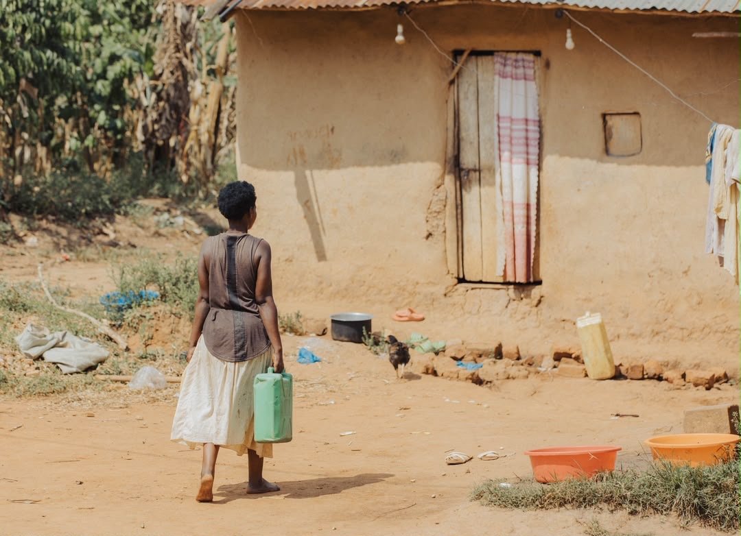 A woman approaching her home carrying a water container