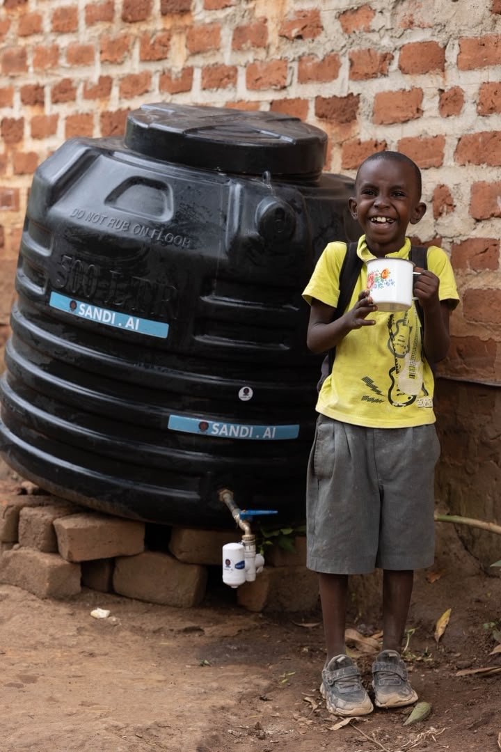 A joyful child holding a drinking cup beside a water tank